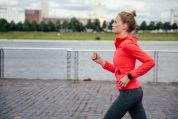 Junge Frau mit roter Jacke joggt am Fluss entlang Junge Frau mit roter Jacke joggt am Fluss entlang